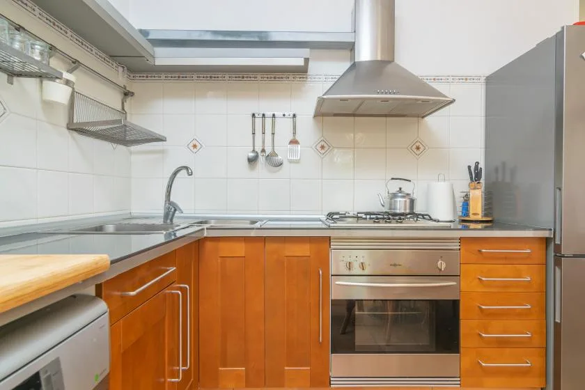 A bright tiled kitchen with wooden cabinets, a counter, and a built-in oven.