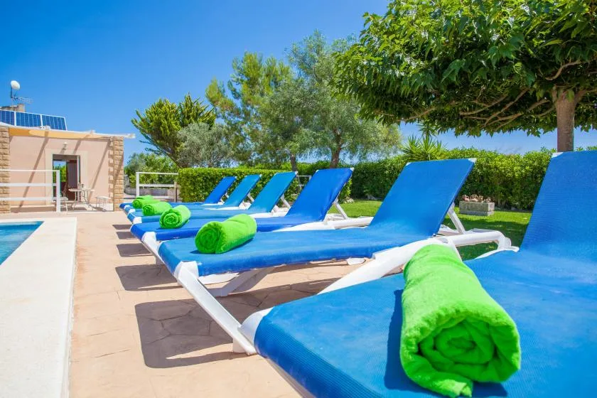 Outdoor poolside seating with blue loungers and bright green towels.