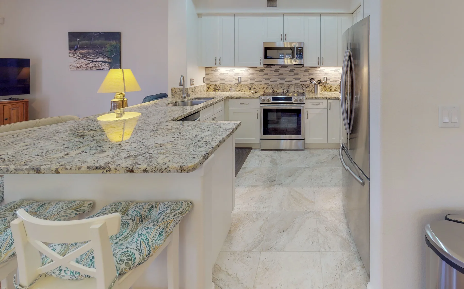 A bright kitchen with a stone countertop, white cabinetry, and stainless steel appliances.