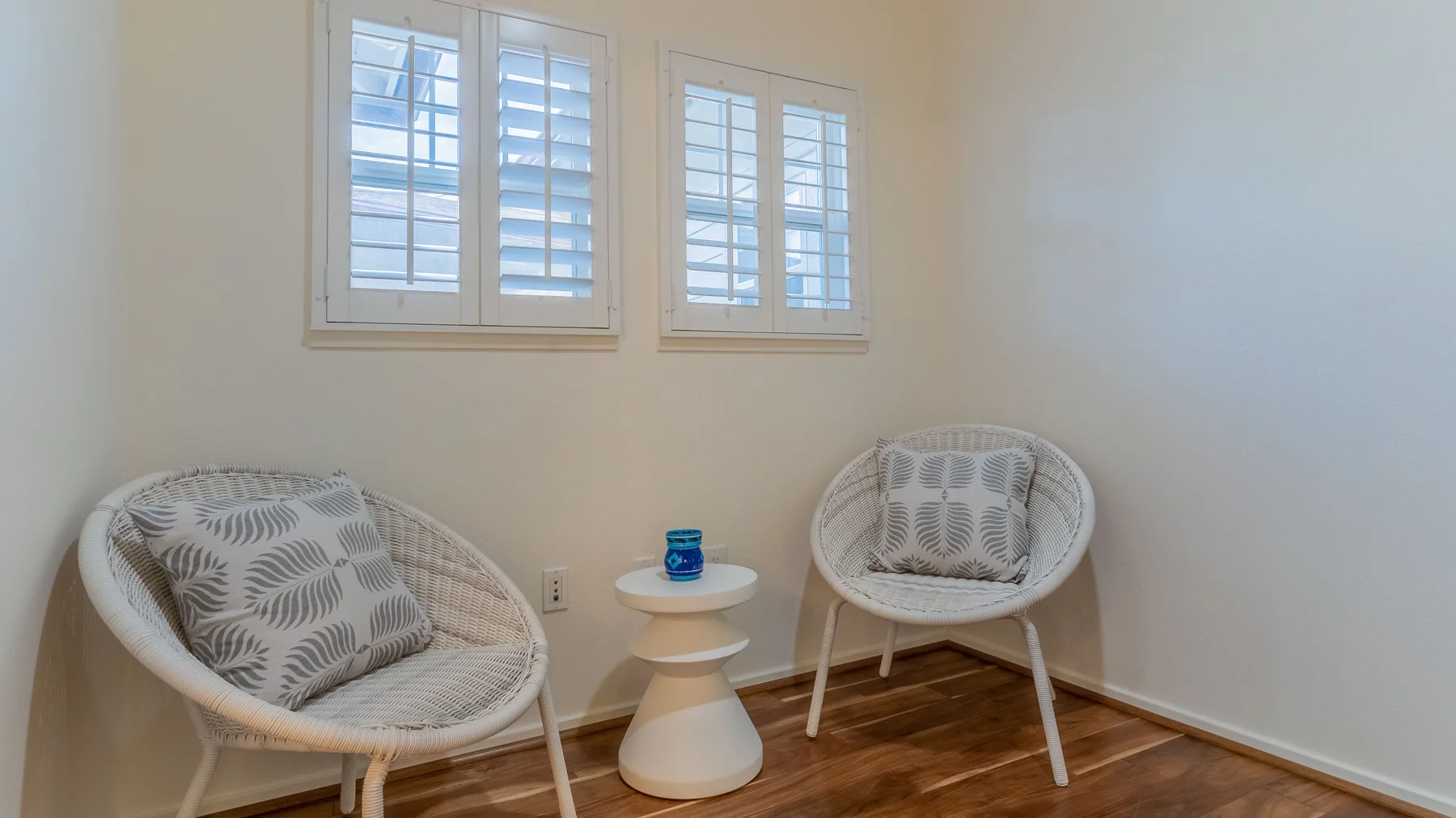 A bright sitting area has two white woven chairs and a small round table.