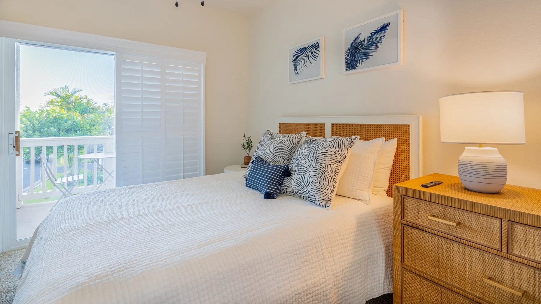 A bright bedroom with a neatly made bed and framed feather prints.