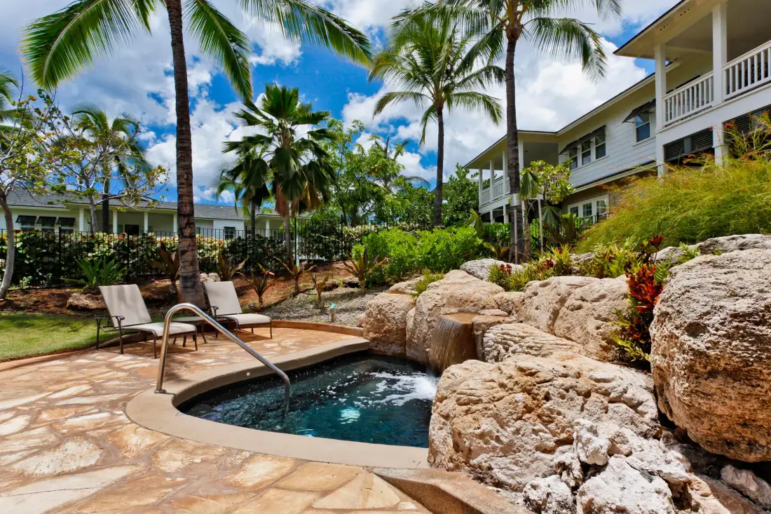 A small outdoor pool sits among rocks, tropical plants, and palm trees.