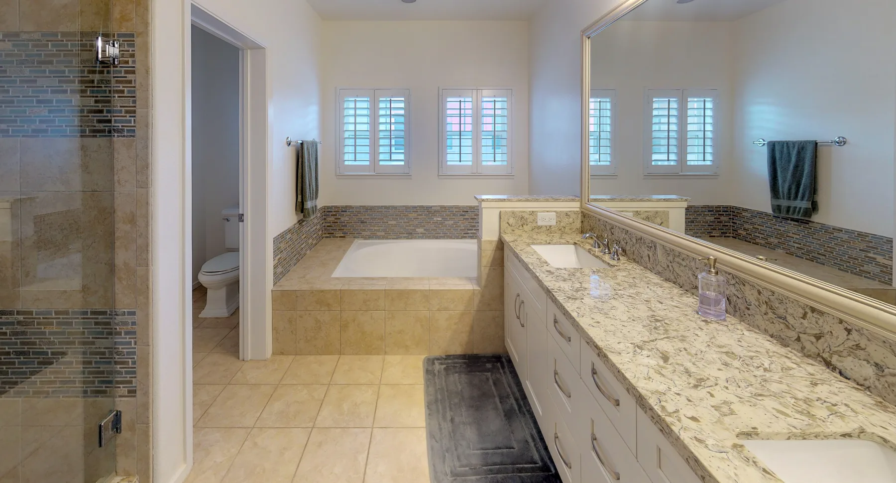 A bright bathroom with a long vanity, large mirror, and separate shower.