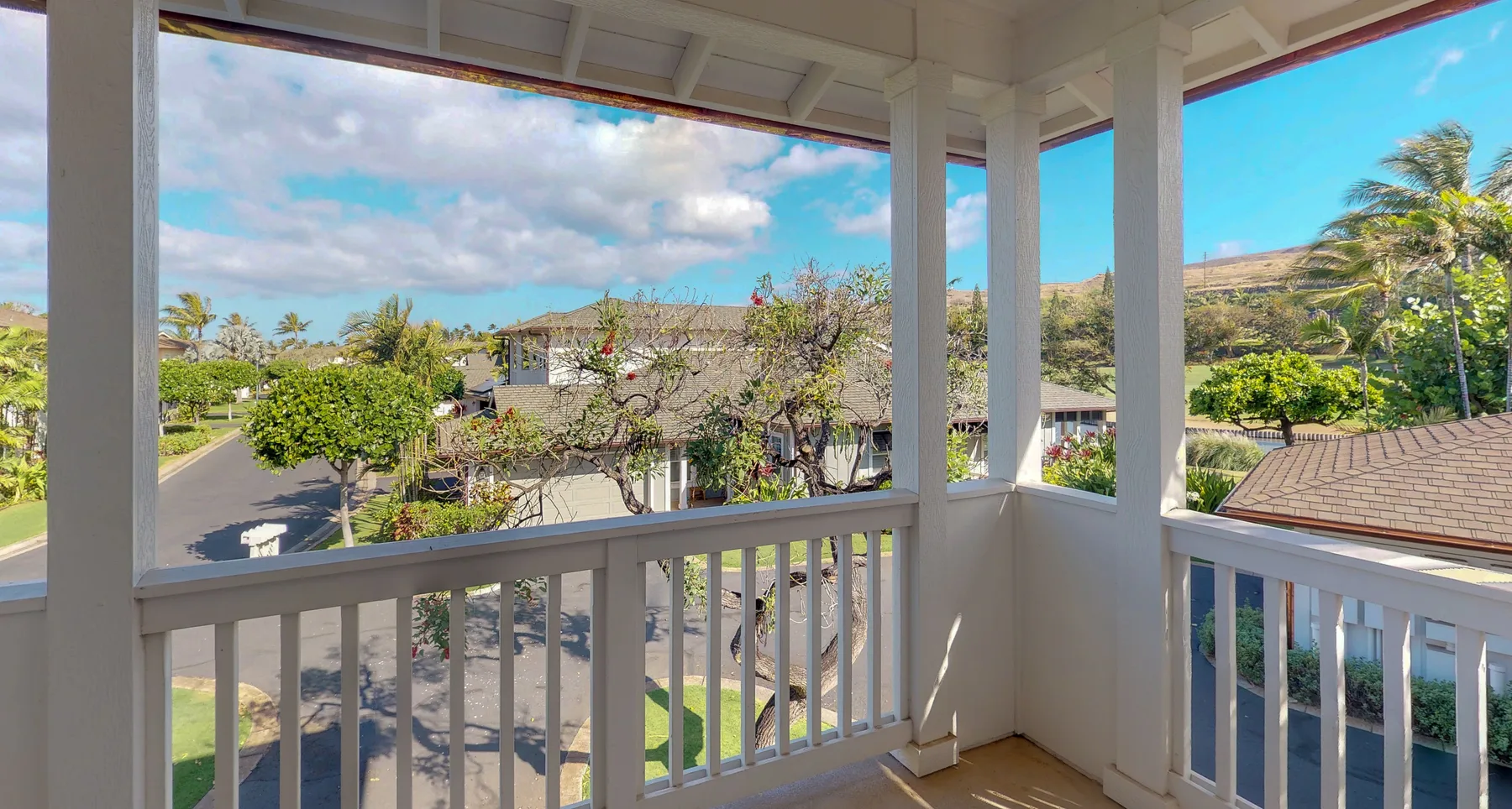 A covered balcony overlooks nearby homes, trees, and a roadway.