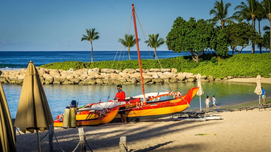 A colorful sailboat rests beside a sandy beach, with a calm lagoon behind it.