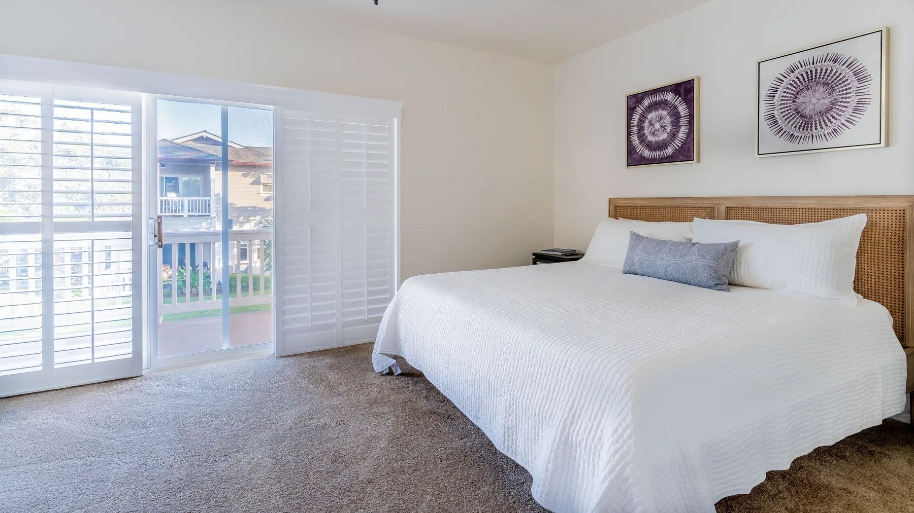 A bright bedroom with a neatly made bed and large windows.