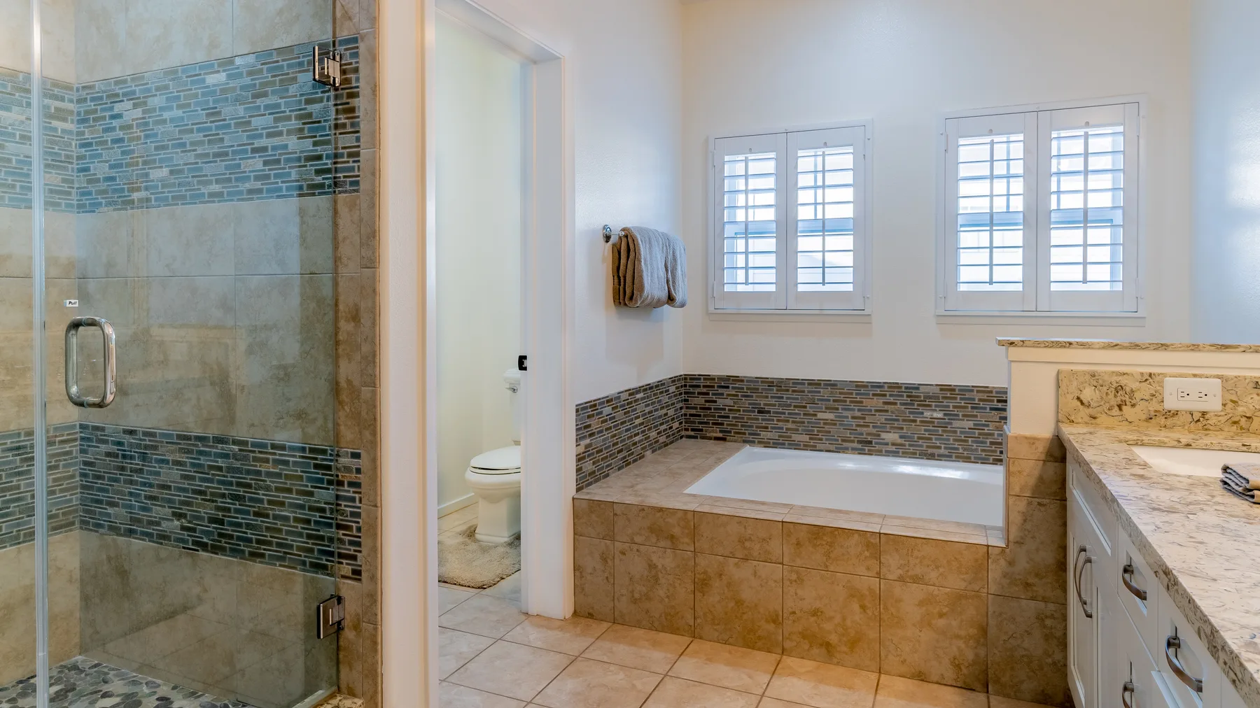 A bright bathroom with a tiled shower, bathtub, and windows.