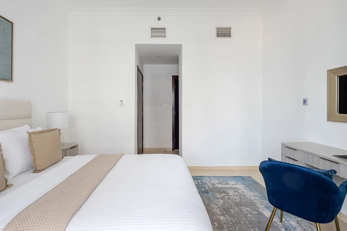 Un dormitorio luminoso con una cama bien hecha y una silla azul.