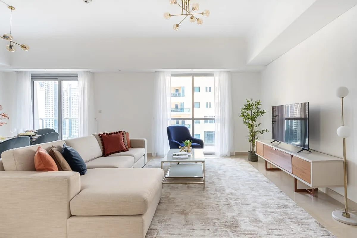 Una sala luminosa con asientos, un televisor y ventanas grandes.