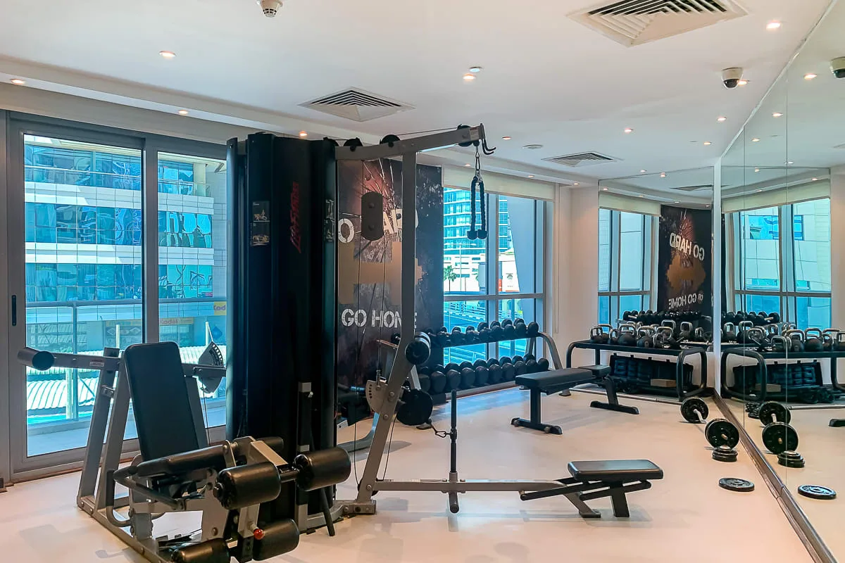 Un gimnasio con máquinas de pesas, mancuernas y grandes ventanas.