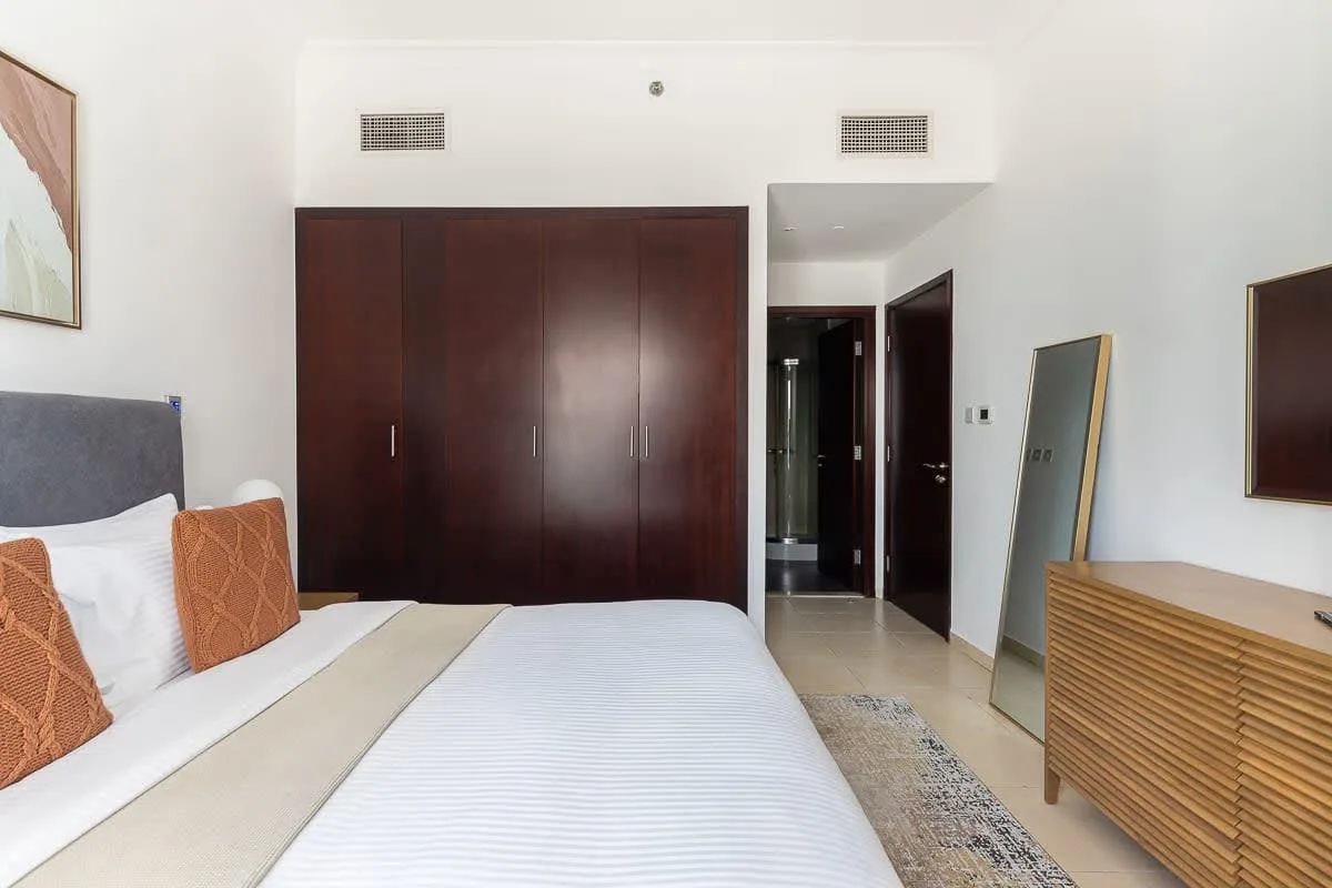 Un dormitorio con una cama tendida, un armario oscuro y una cómoda.