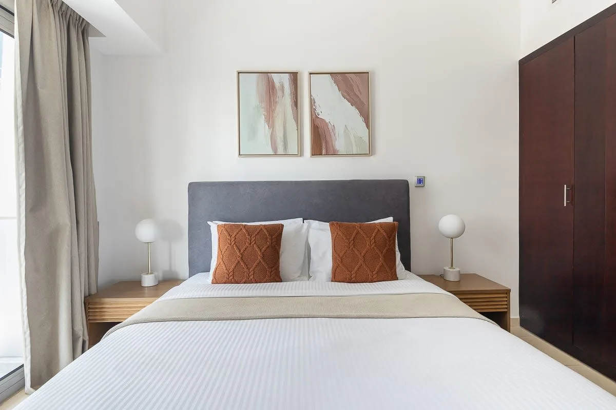 Un dormitorio con una cama bien hecha, cojines decorativos y cuadros sobre el cabecero.