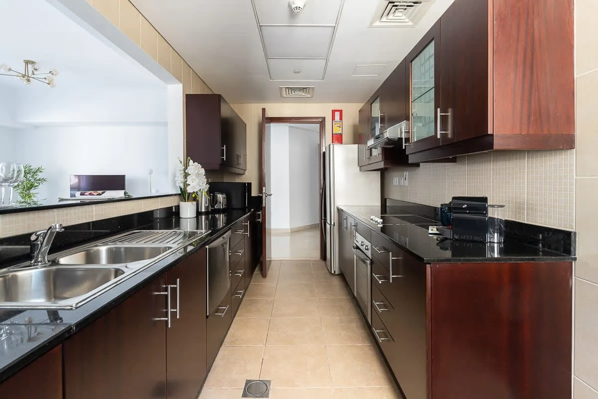 Una cocina estrecha con gabinetes oscuros, encimeras negras y electrodomésticos de acero inoxidable.