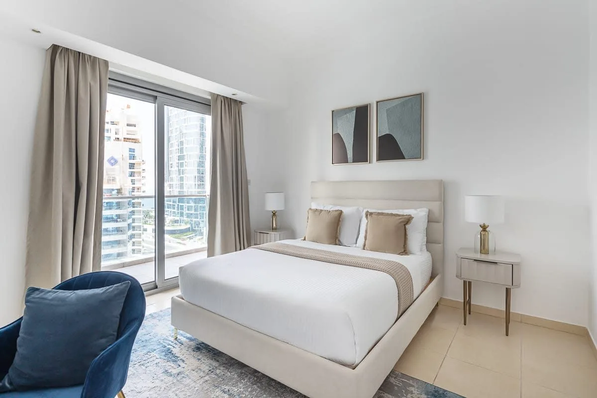 Un dormitorio luminoso con una cama bien arreglada y grandes ventanales.