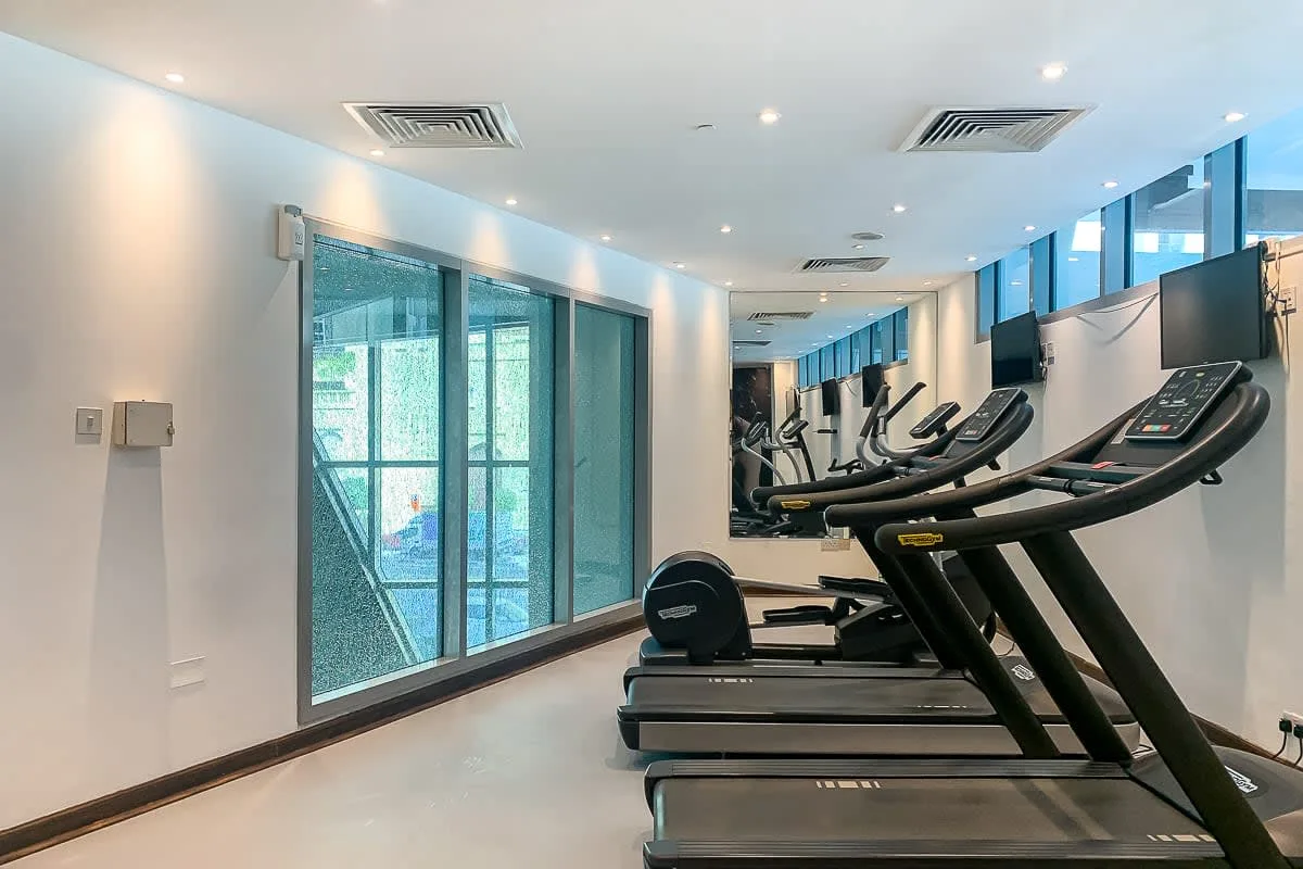 Un gimnasio con cintas de correr junto a grandes ventanales.