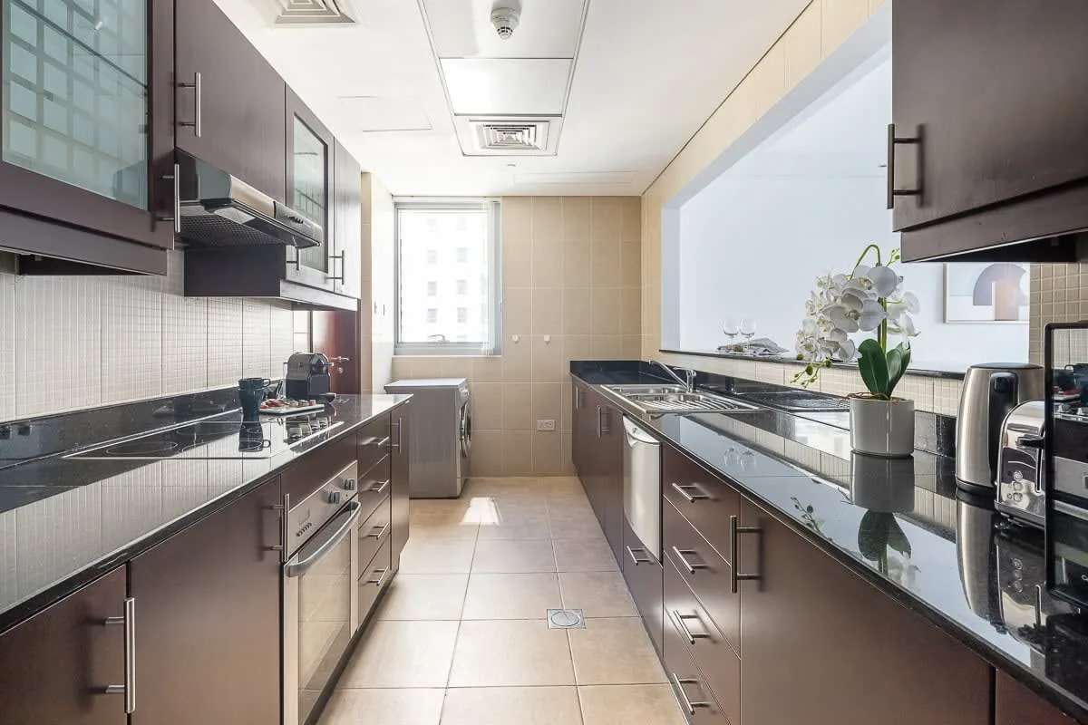 Una cocina moderna y luminosa tiene gabinetes oscuros, encimeras largas y una ventana al fondo.