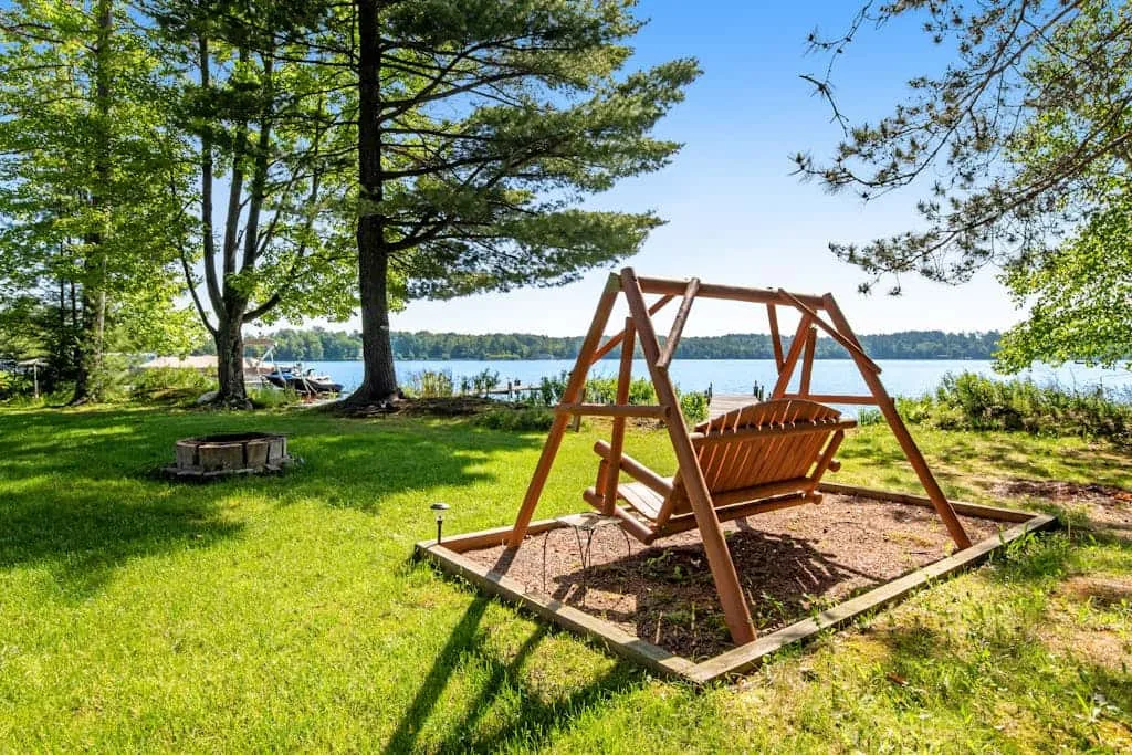 Un columpio de madera está en un césped junto a un lago.