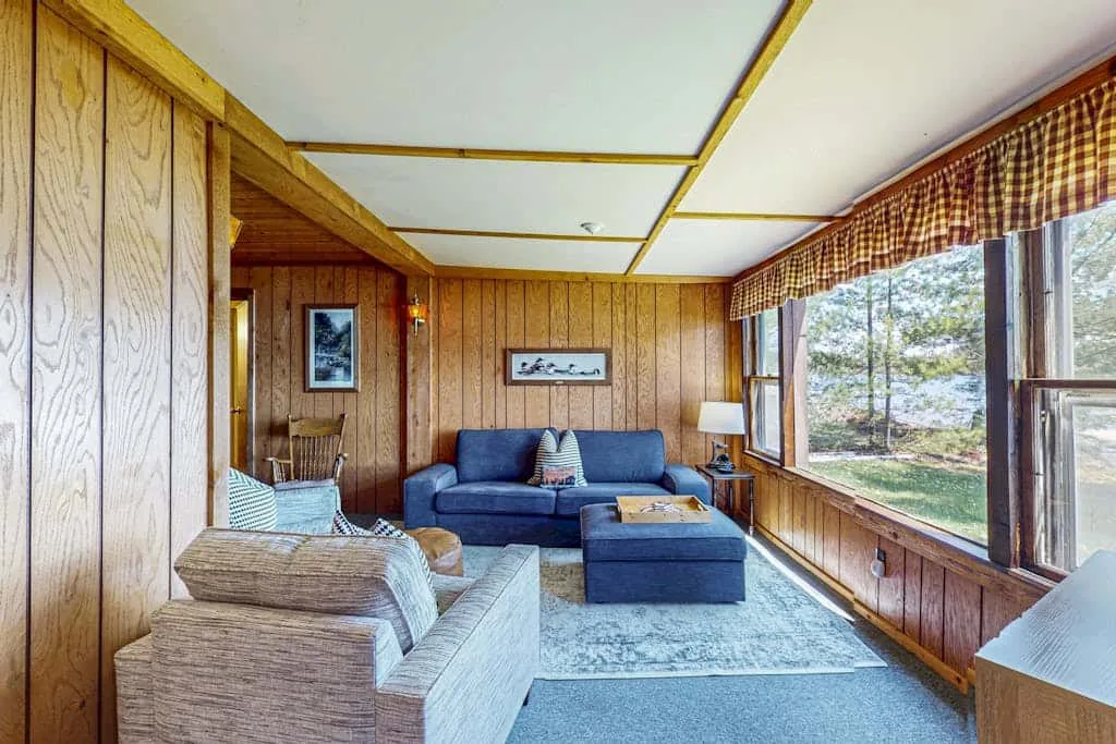 Una sala de estar revestida de madera con asientos junto a grandes ventanas.