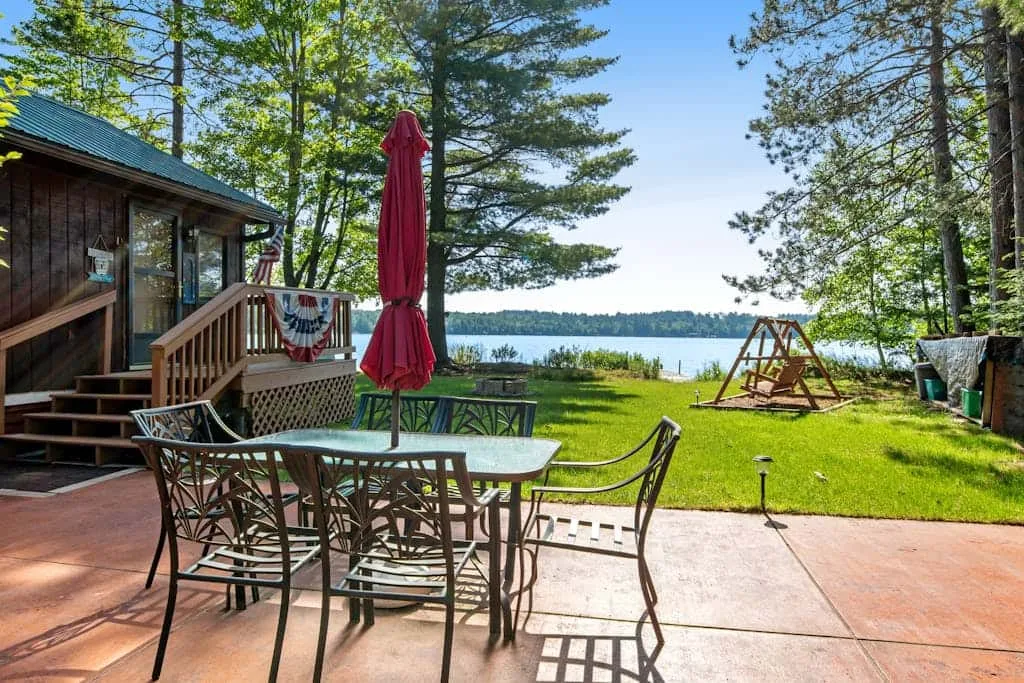 A lakeside patio with outdoor seating, a closed umbrella, and a view of the water.
