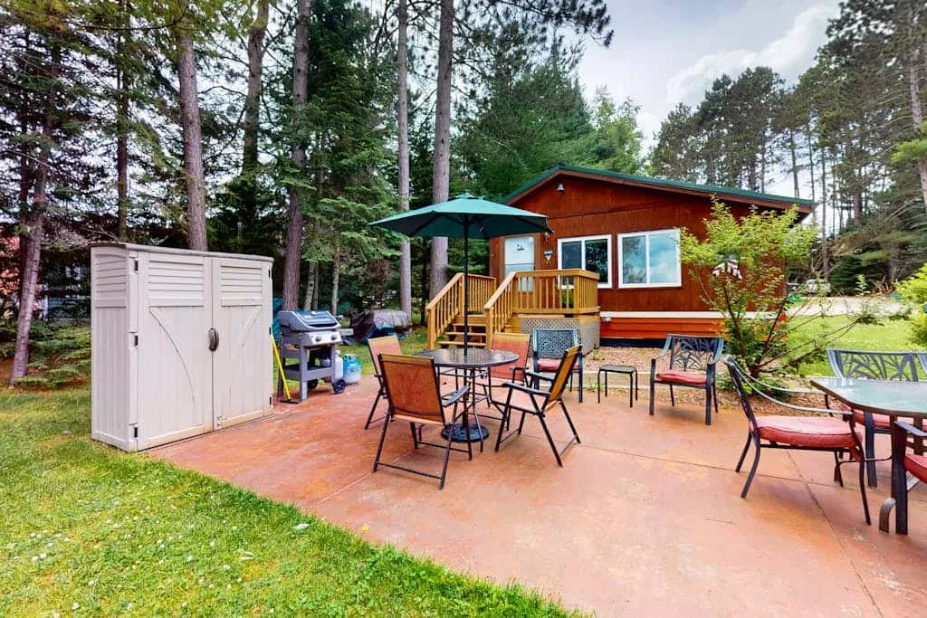 Un patio exterior con asientos y una sombrilla junto a una pequeña cabaña.