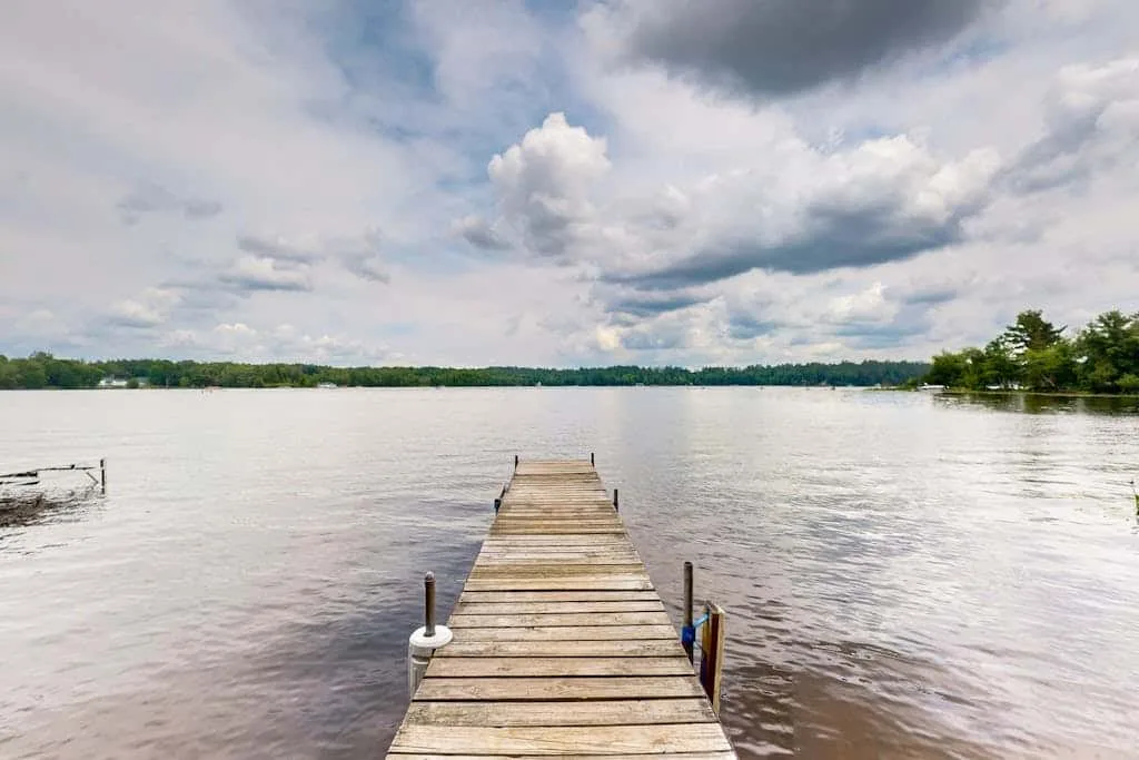 Un muelle de madera se extiende sobre un lago bajo un cielo nublado.