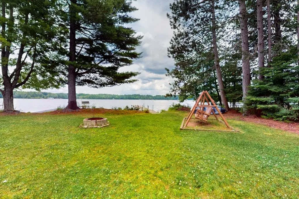 Un patio junto al lago, con césped y un columpio de madera bajo árboles altos.