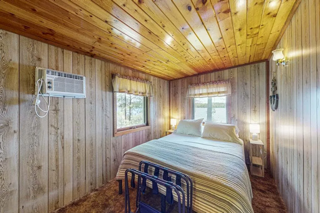 Un dormitorio con una cama bajo un techo de madera y ventanas.