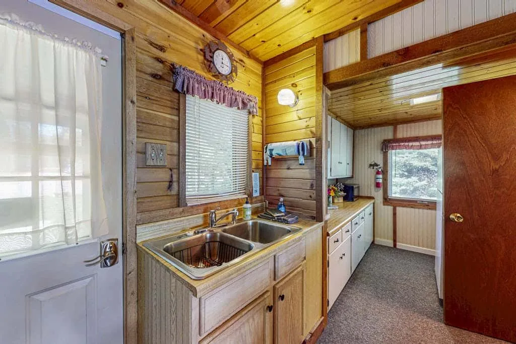 Una cocina compacta con fregadero de dos senos, armarios de madera y una ventana.