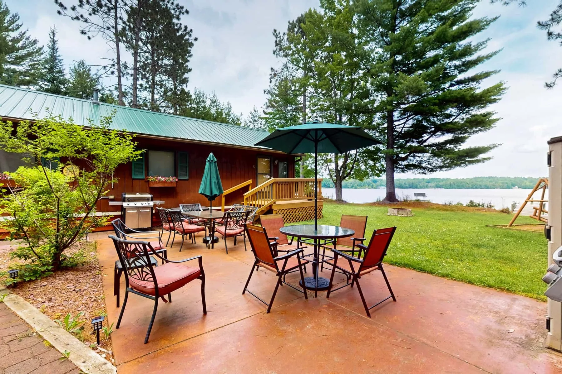 Un patio al aire libre con mesas y sillas junto a un edificio de madera, con vistas a un lago.