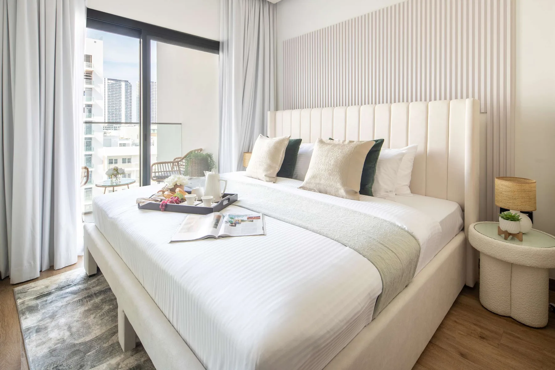 Un dormitorio luminoso con una cama grande, una pared de rayas claras y ventanales.