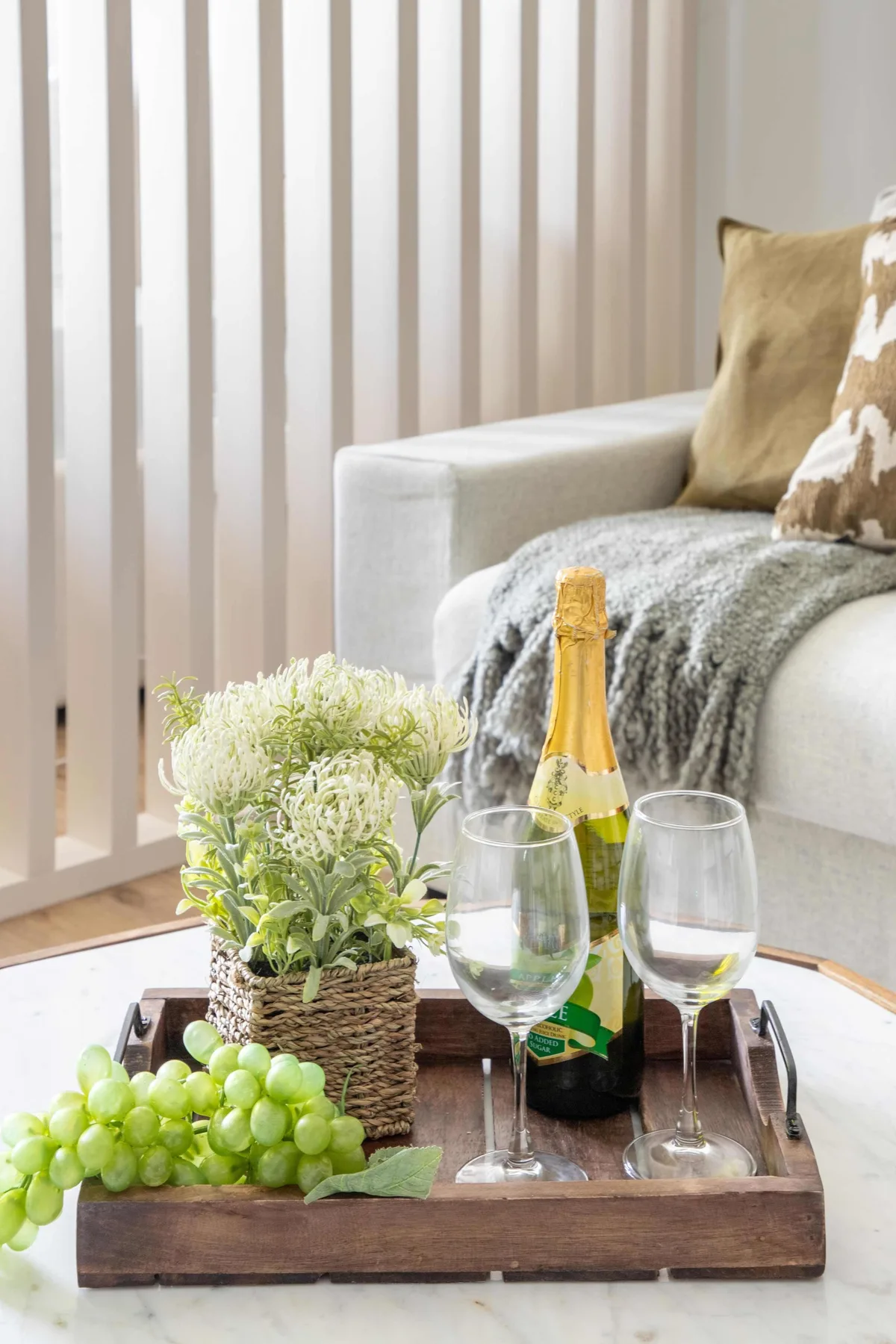 A living room seating area with a wooden tray, sparkling wine, and grapes.