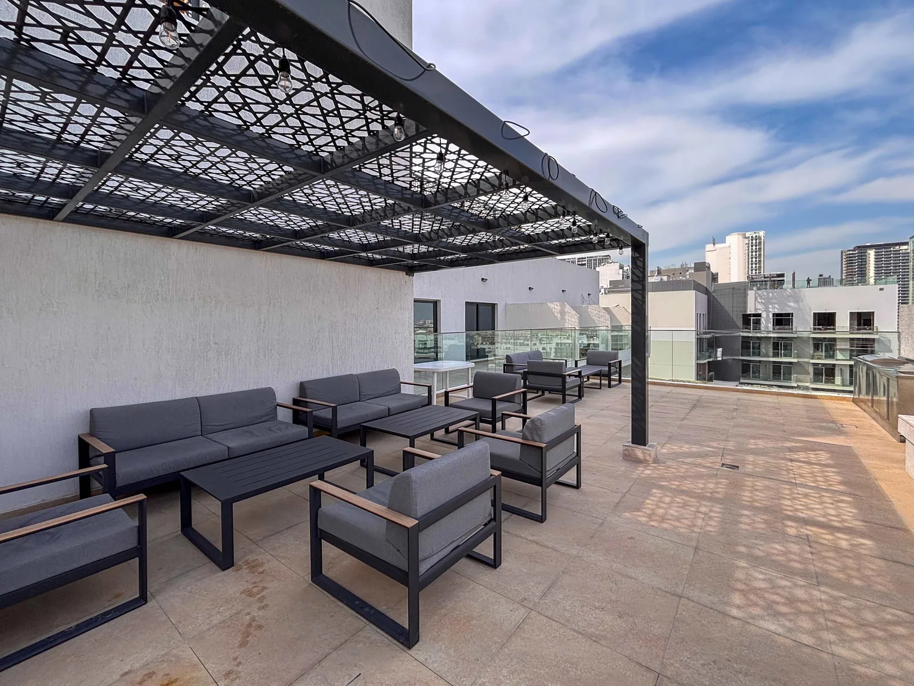 Una terraza en la azotea tiene asientos al aire libre bajo una pérgola negra de celosía.