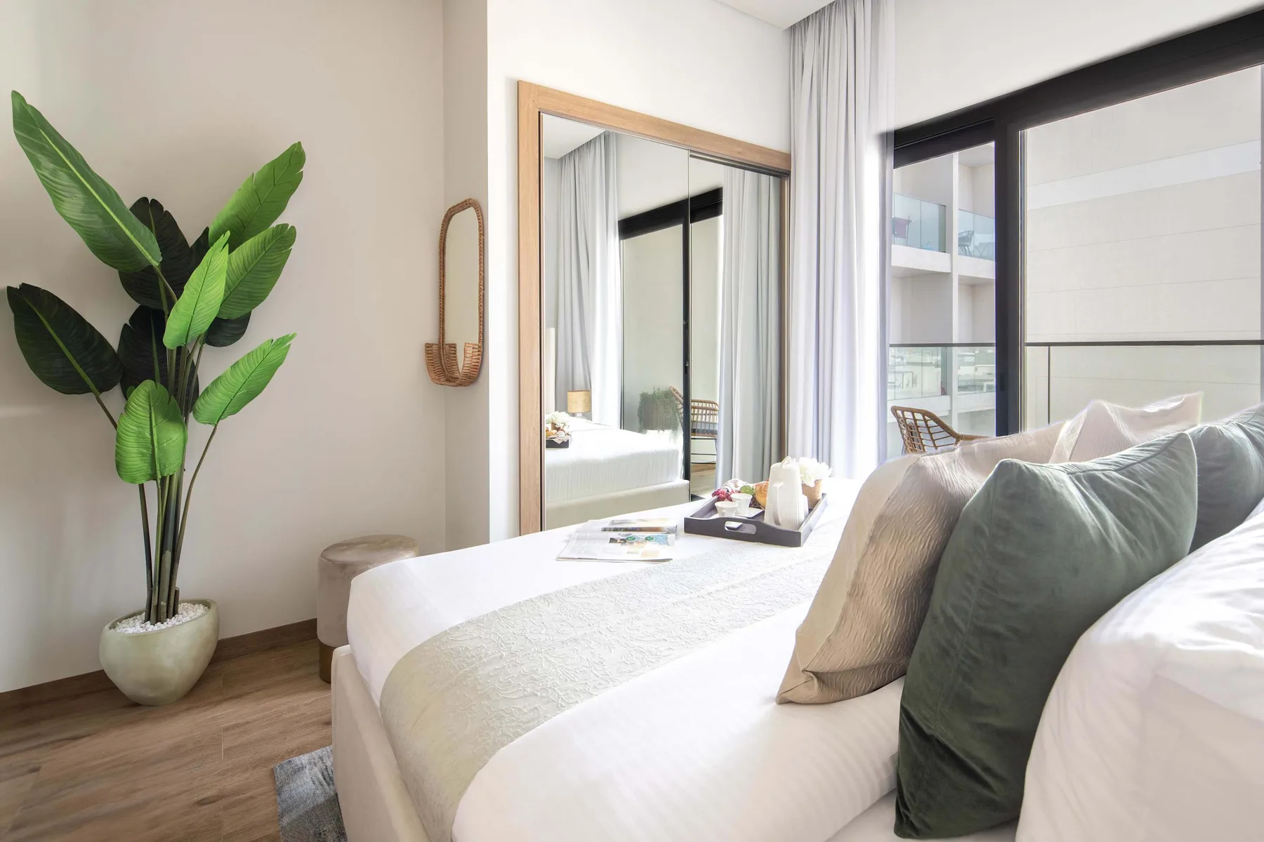 Un dormitorio luminoso con una cama bien tendida y una planta alta de hojas verdes.