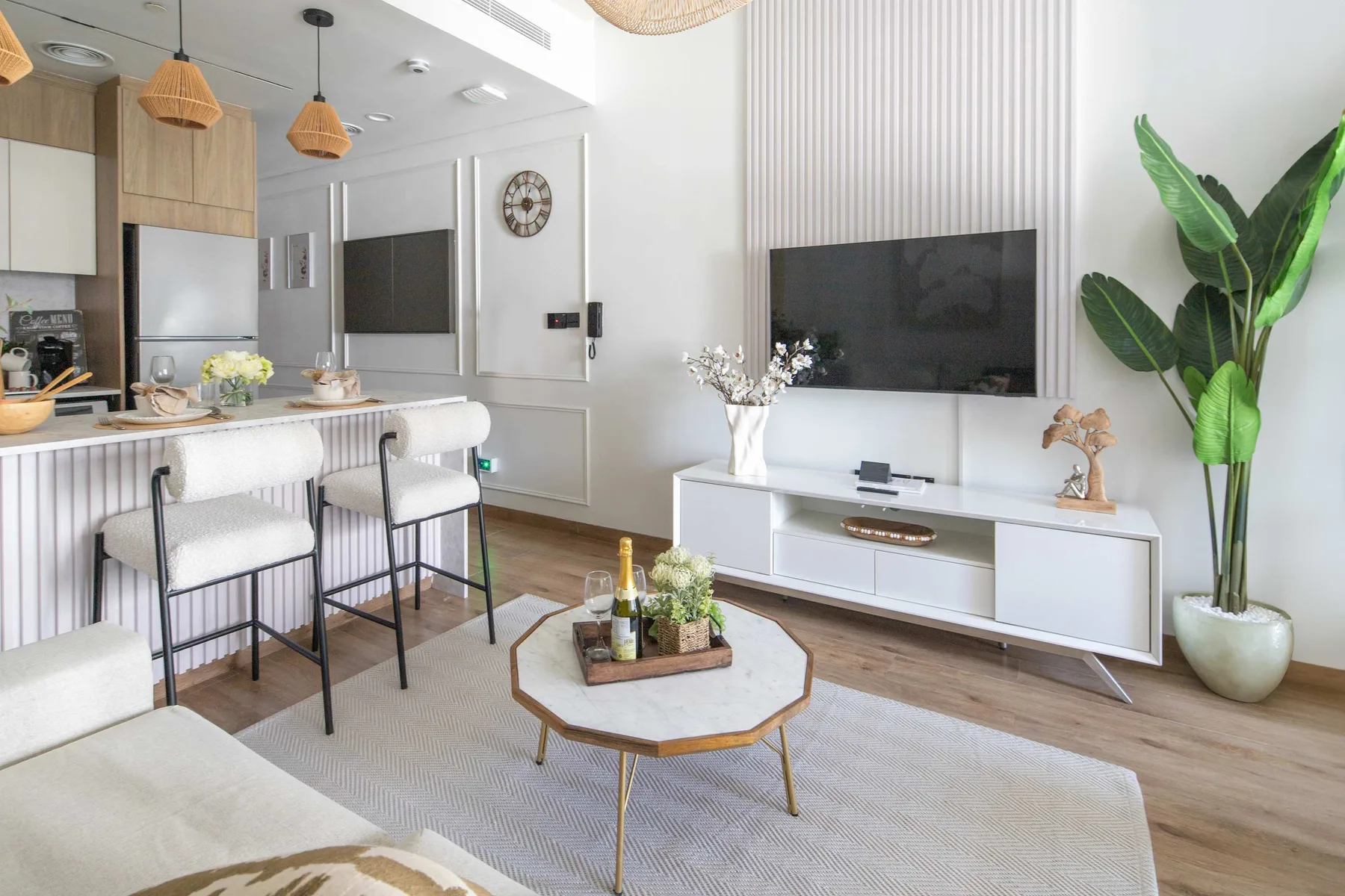 Una sala luminosa con televisor, asientos junto a la barra y una mesa de centro.