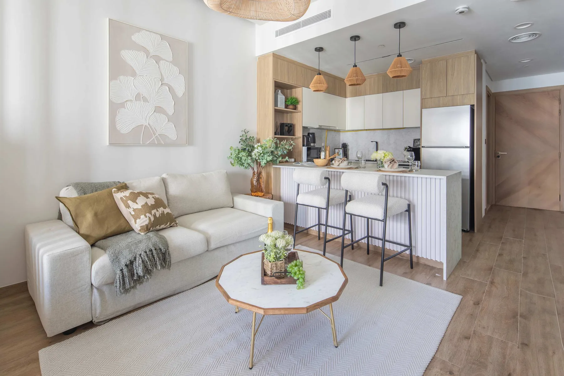 Una luminosa sala de estar se abre a una cocina, con sofá y barra de desayuno.