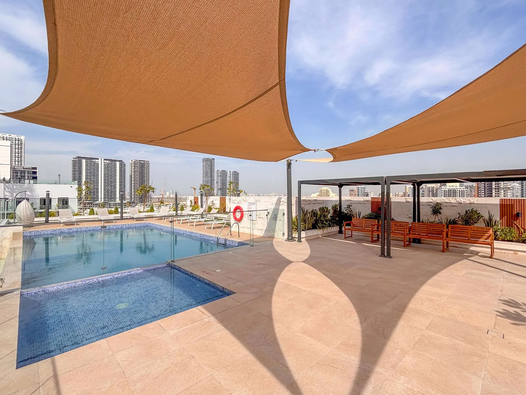 Una piscina exterior y una terraza pavimentada están bajo grandes toldos de sombra.
