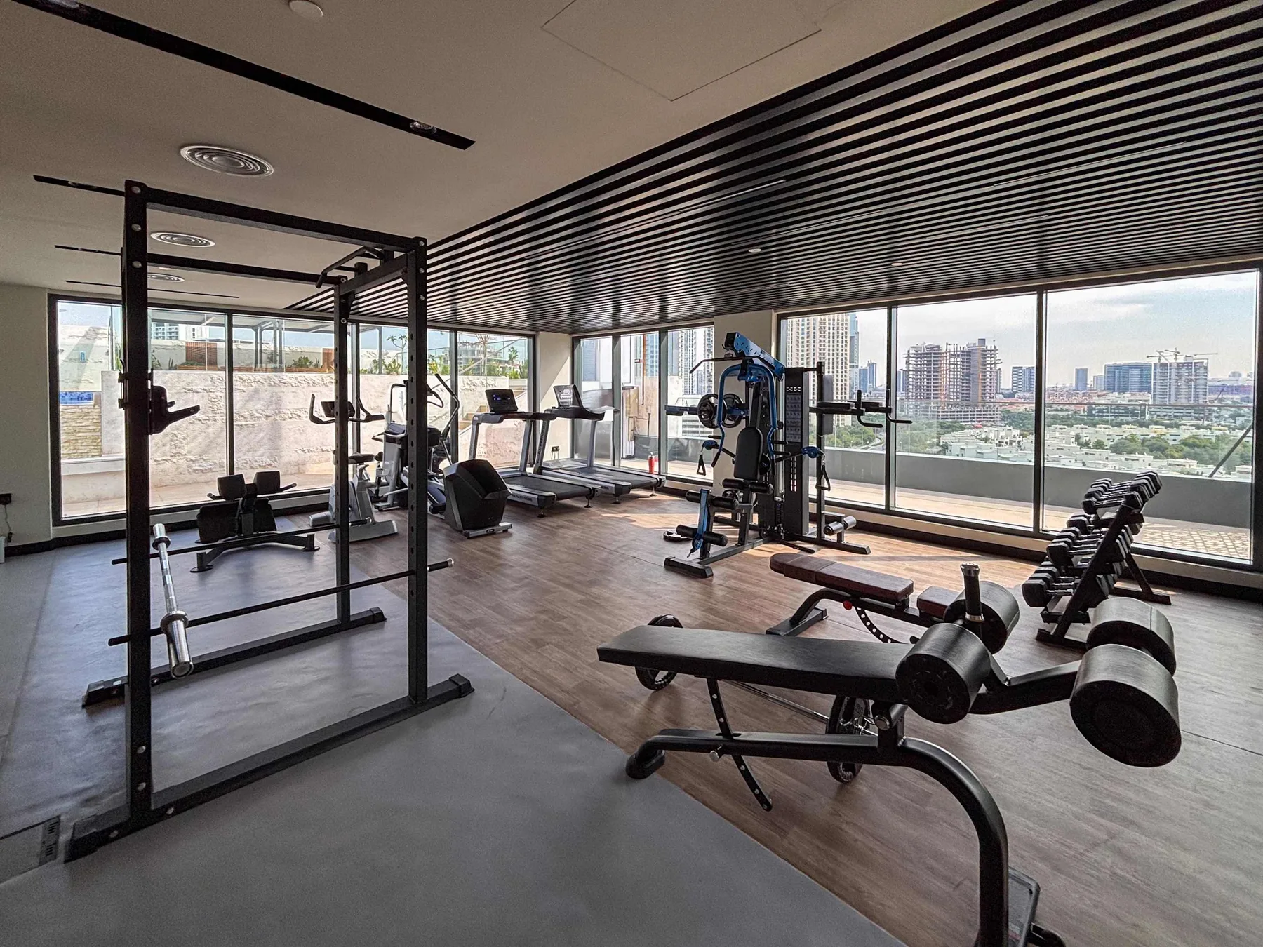 Un gimnasio con máquinas de pesas y equipo de ejercicio junto a grandes ventanas.