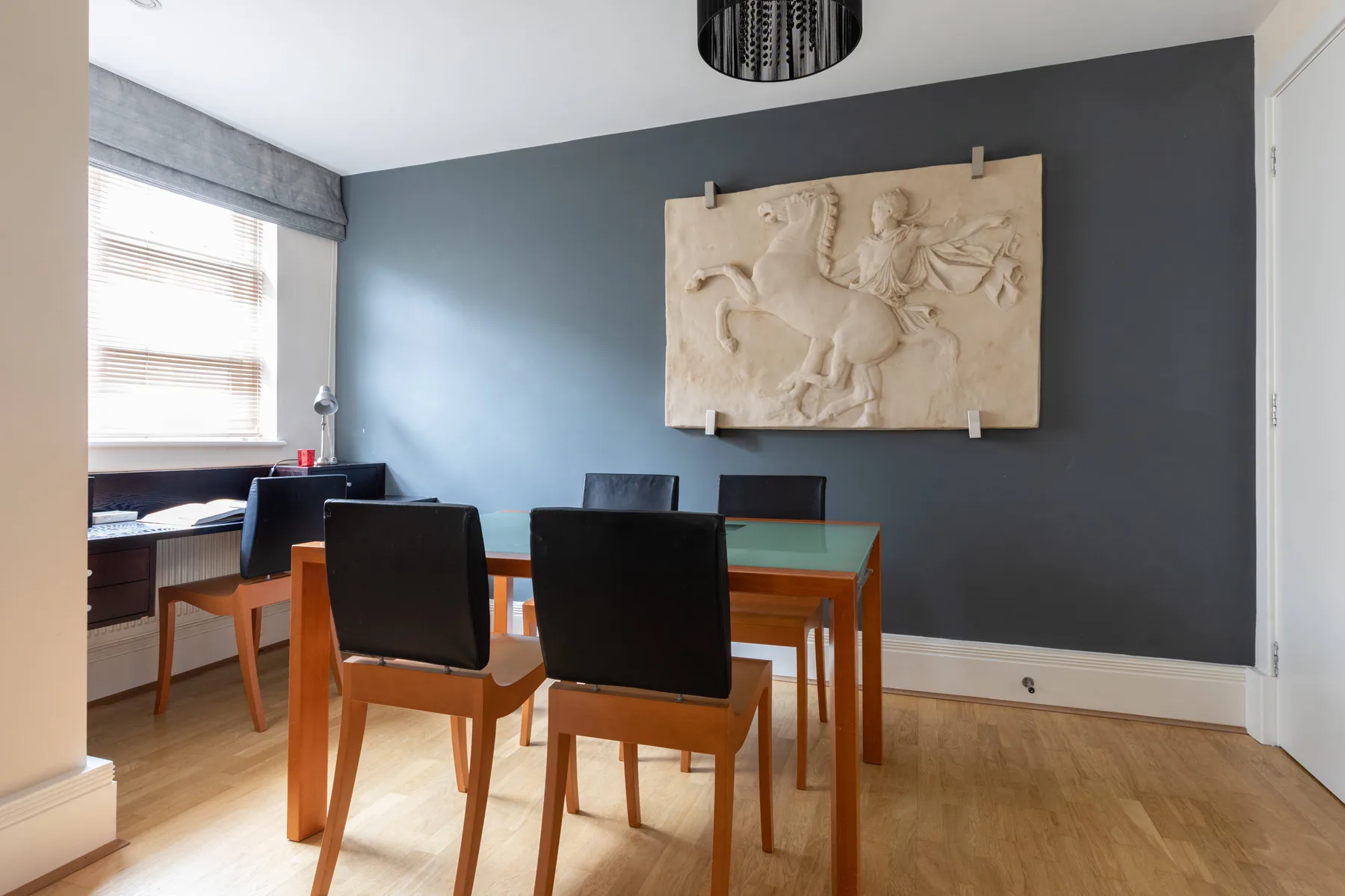Un comedor con una mesa de madera y sillas frente a una pared gris.