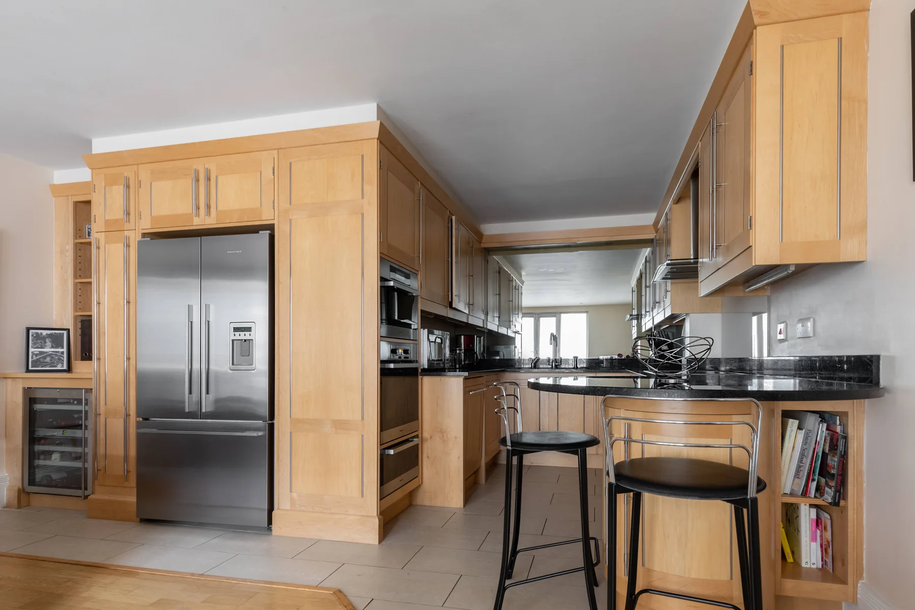 Una cocina con gabinetes de madera clara, electrodomésticos de acero inoxidable y una barra para desayunar.