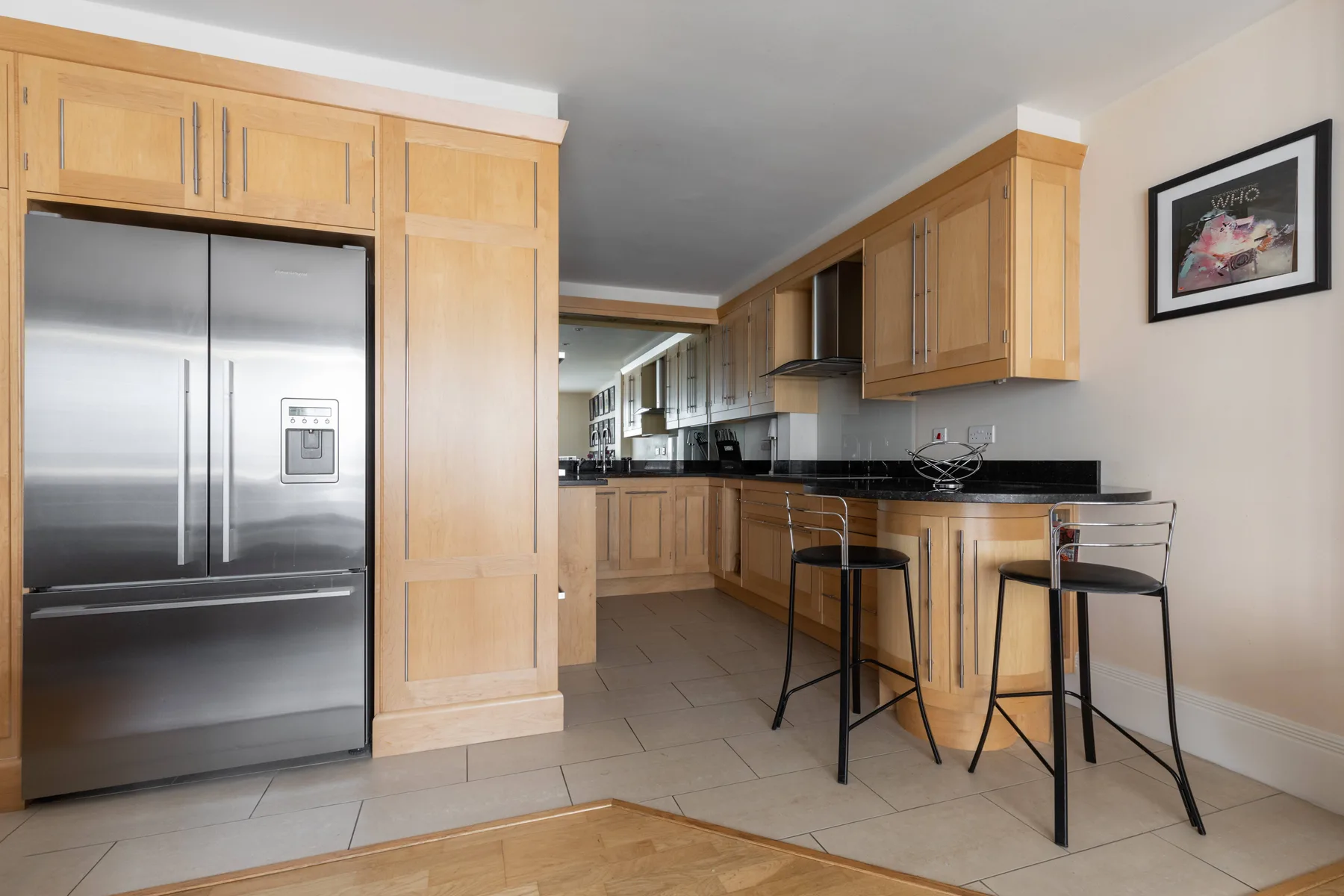 Una cocina con gabinetes de madera clara, un refrigerador de acero inoxidable y una barra.
