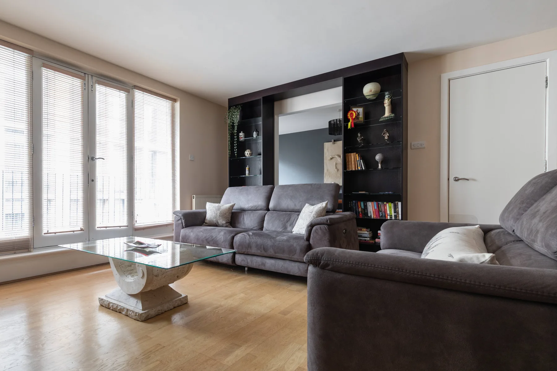 Una sala de estar con asientos grises, una mesa de centro de vidrio y ventanas altas.