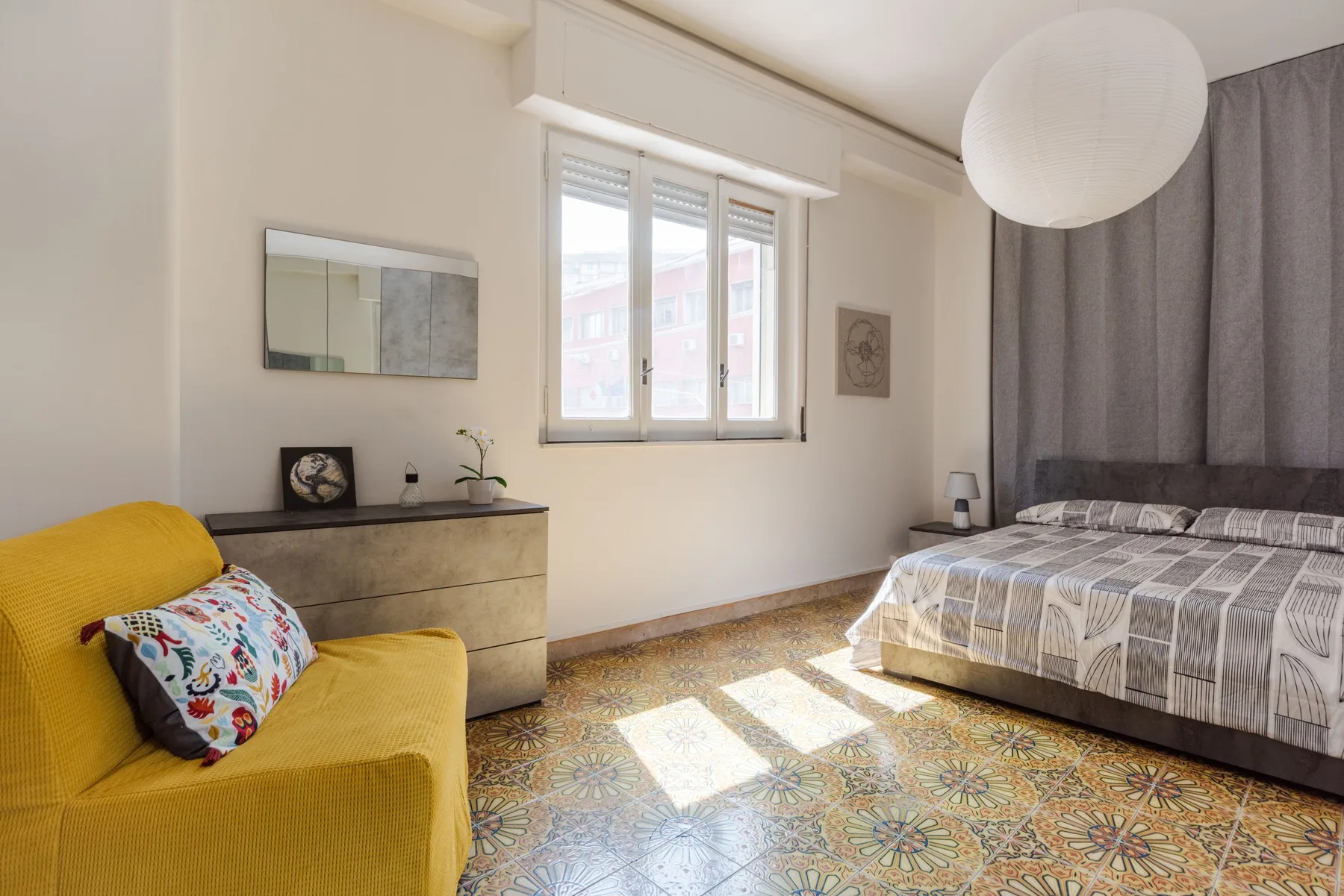 A bedroom with a bed, yellow seating, and a window overlooking the street.