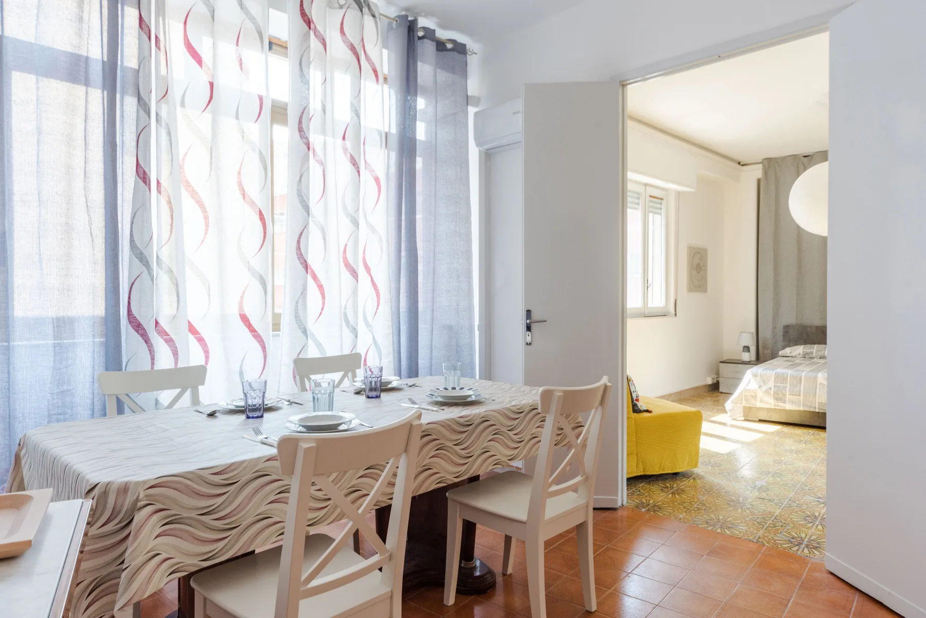Un comedor con una mesa y sillas junto a ventanas altas con cortinas.