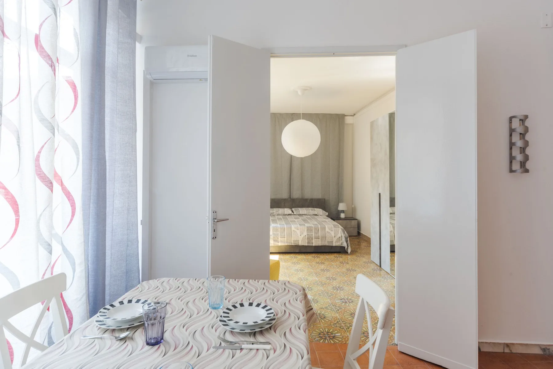 A dining area with a set table looks through open doors into a bedroom.