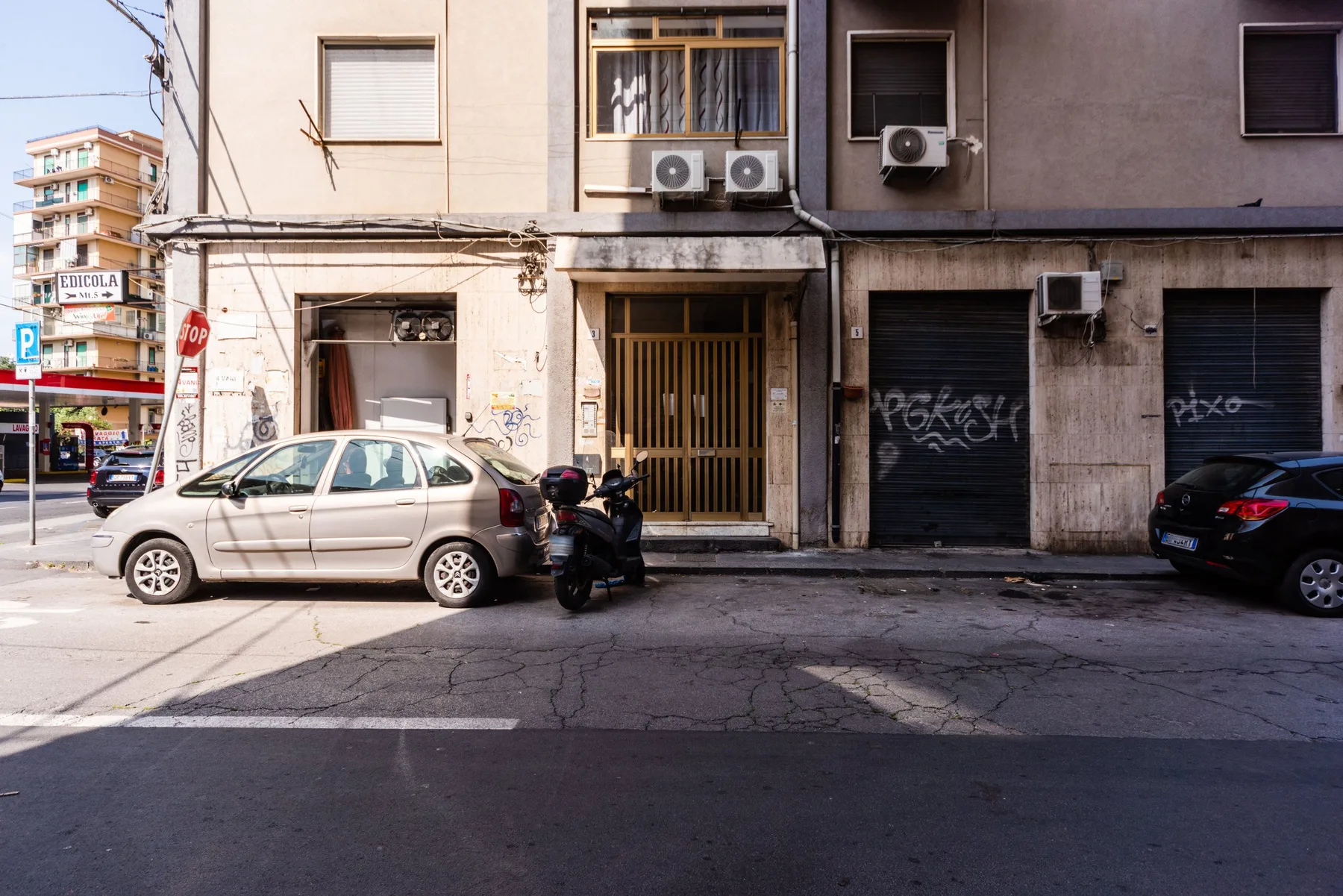 Street-facing building entrance between shuttered storefronts, with parked vehicles along the curb.