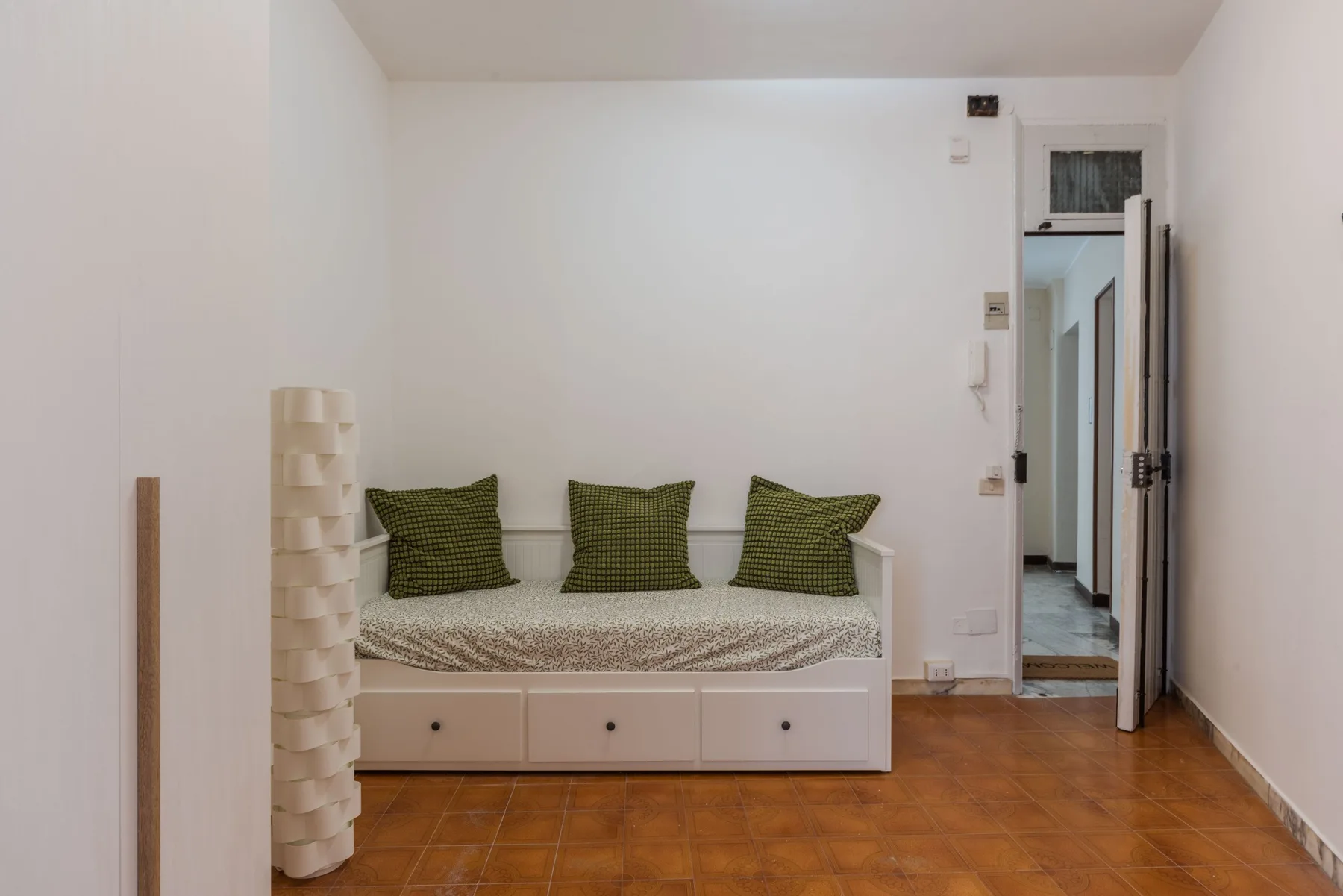 A daybed with green cushions sits against the wall beside an open doorway.