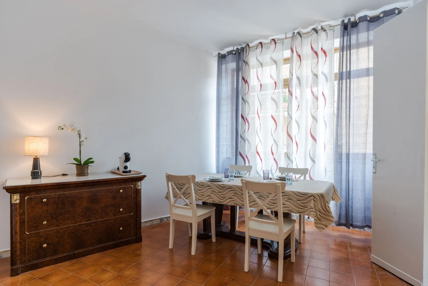 A dining area with a table and chairs beside a window with patterned curtains.