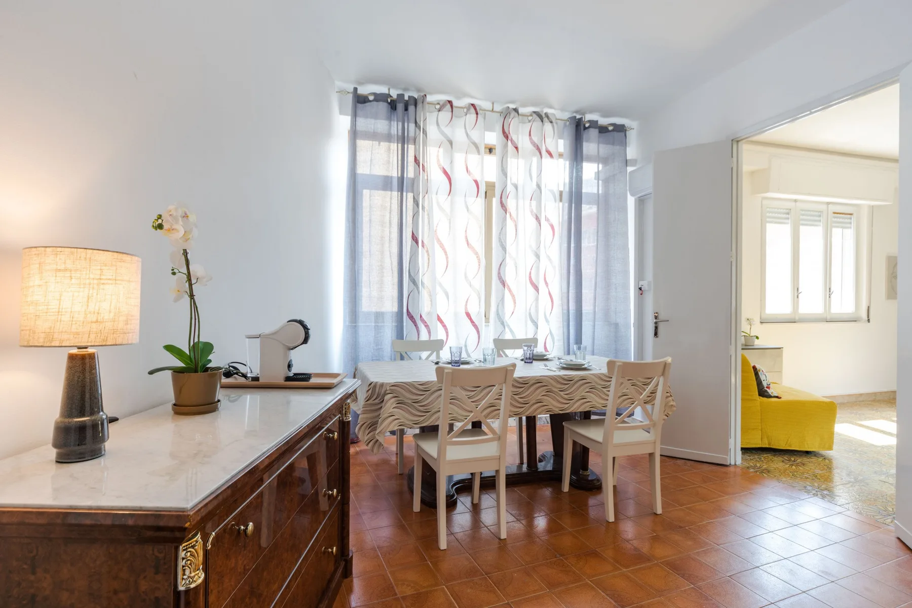 A bright dining area has a wooden table and chairs beside a sunlit window.