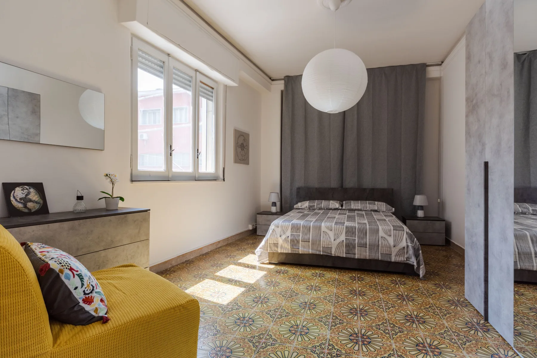 A bedroom with a bed, gray curtains, and a yellow seating area.