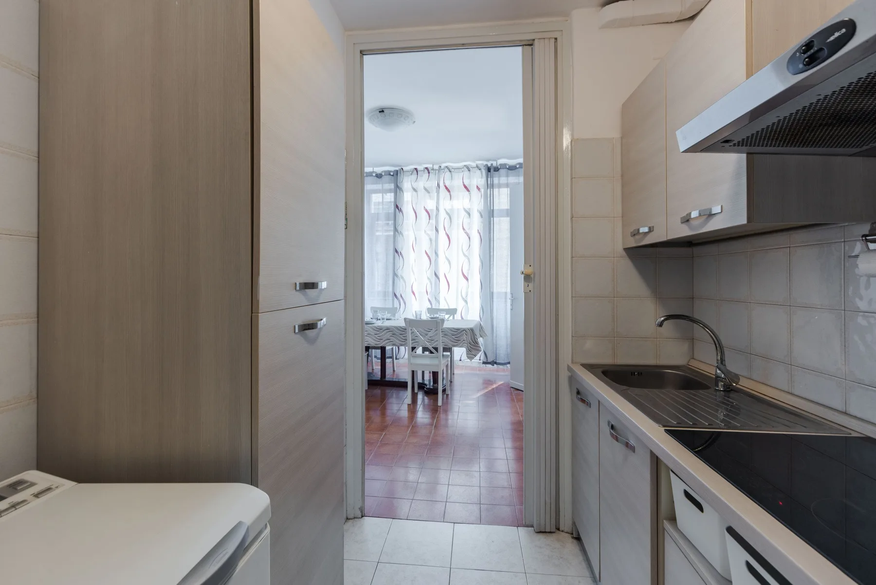 A narrow kitchen with a countertop and sink opens into a bright dining area.